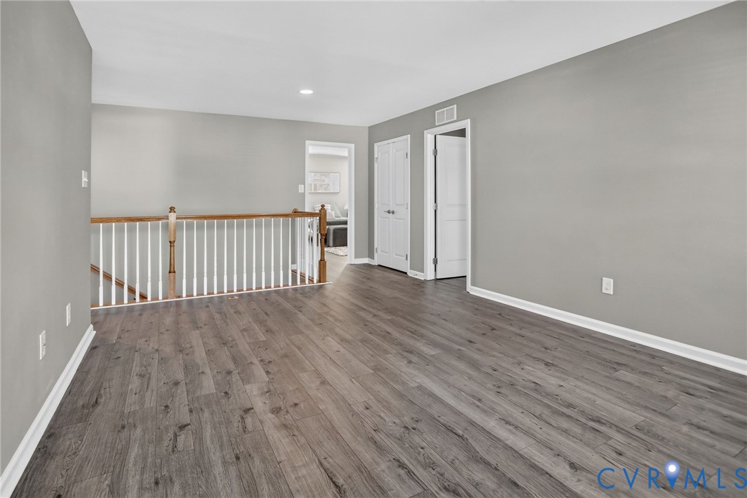 Interior space featuring wood-finish flooring, neutral wall paint, and a staircase landing with a stained-wood railing and white balusters