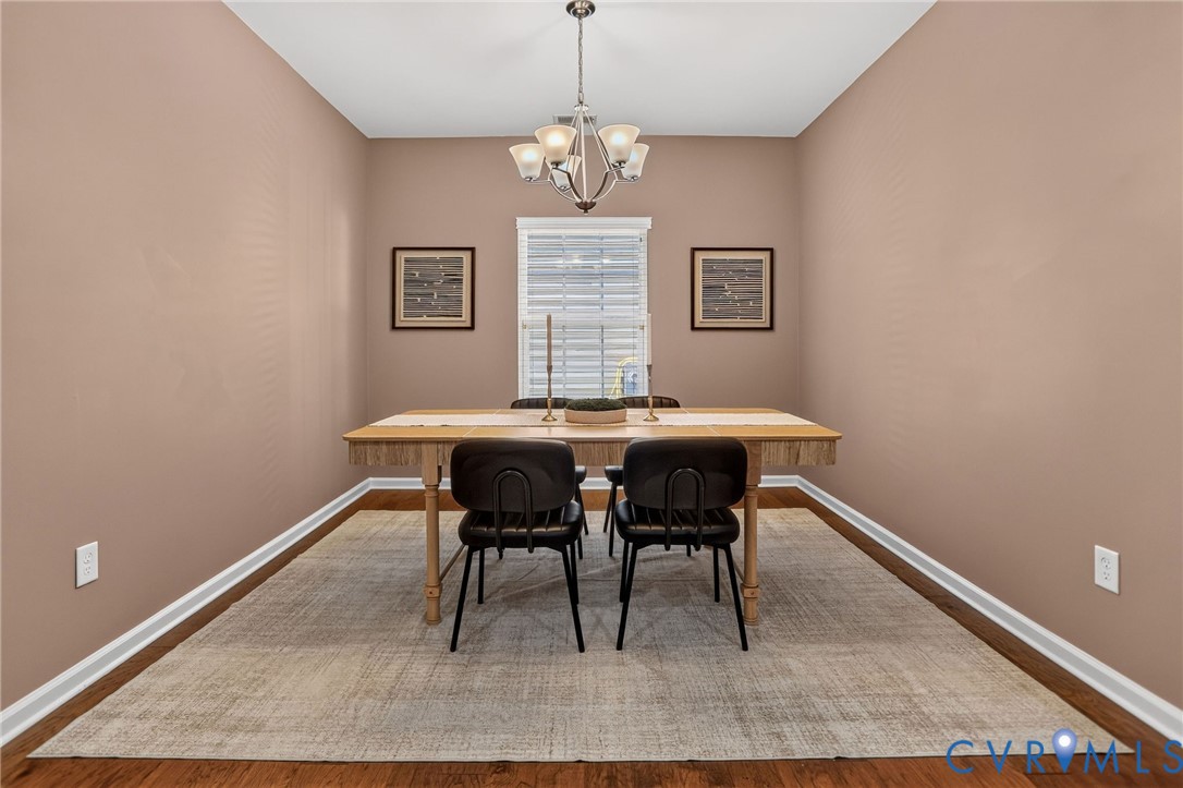 Dining space featuring wood-finish flooring, a central multi-arm metal chandelier, and a single window with blinds Dining space featuring wood-finish flooring, a central multi-arm metal chandelier, and a single window with blinds