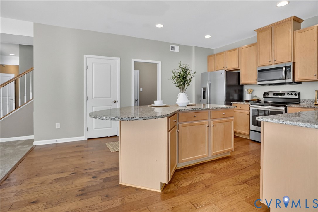 Kitchen featuring wood-finish flooring, stone-surface countertops, wood cabinetry, stainless steel appliances, and a central island with an extended counter