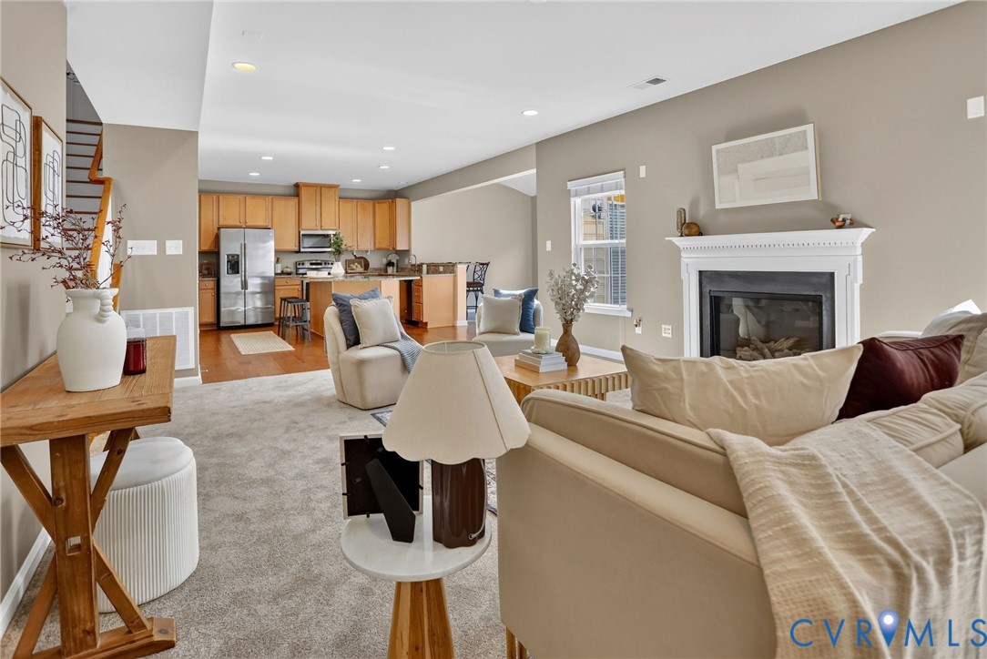 Open-concept living space featuring a white mantel fireplace, recessed lighting, wood-finish cabinetry, and a kitchen island