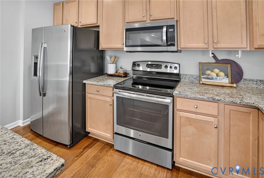 Kitchen featuring stainless steel appliances, natural-finish wood cabinetry, stone-surface countertops, and wood-finish flooring