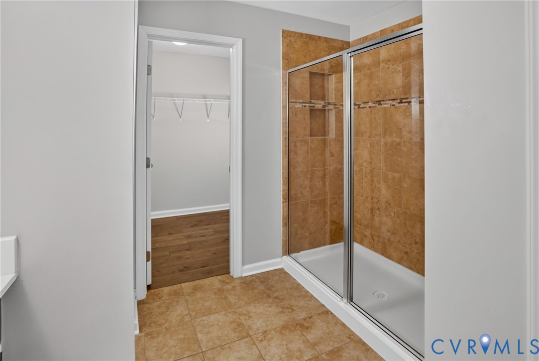 Walk-in shower with floor-to-ceiling tile surround, decorative accent inlay, built-in shelving, and a metal-framed glass enclosure, complemented by tile flooring