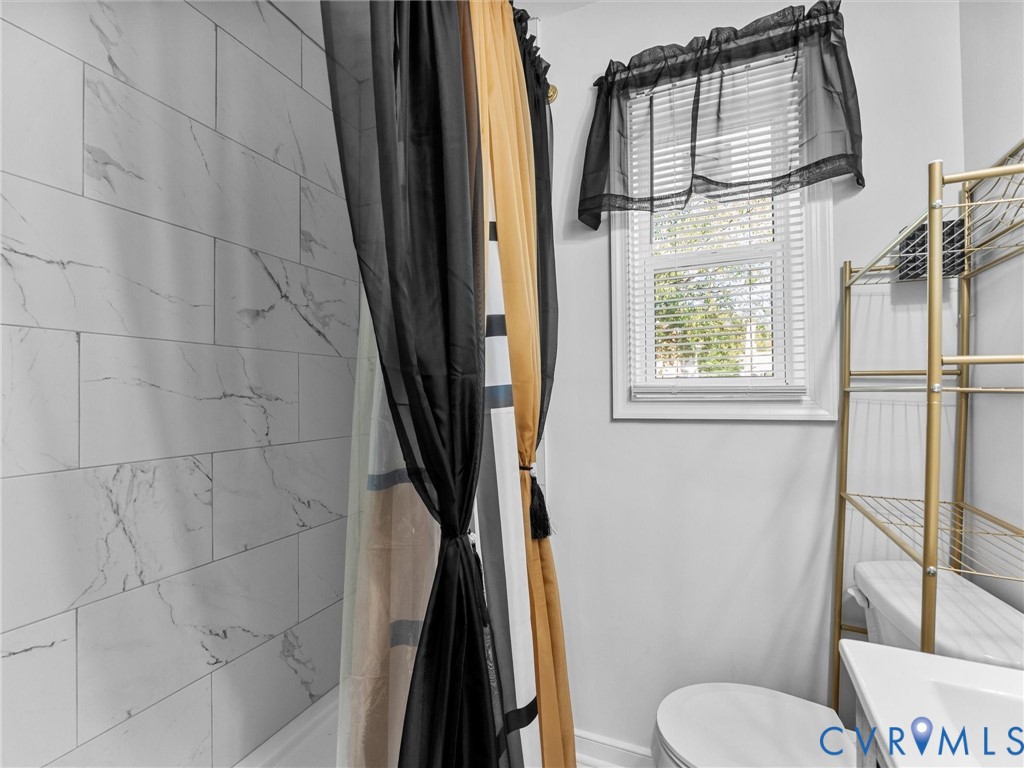 Bathroom featuring wall-to-wall large format rectified tile with a veined pattern, window with horizontal blinds, and a white sink