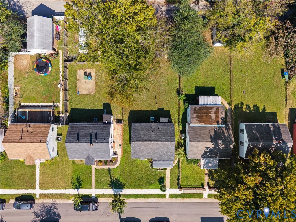 Aerial perspective of a residential block featuring gable-roofed structures, expansive lawn areas, mature trees, and paved street access