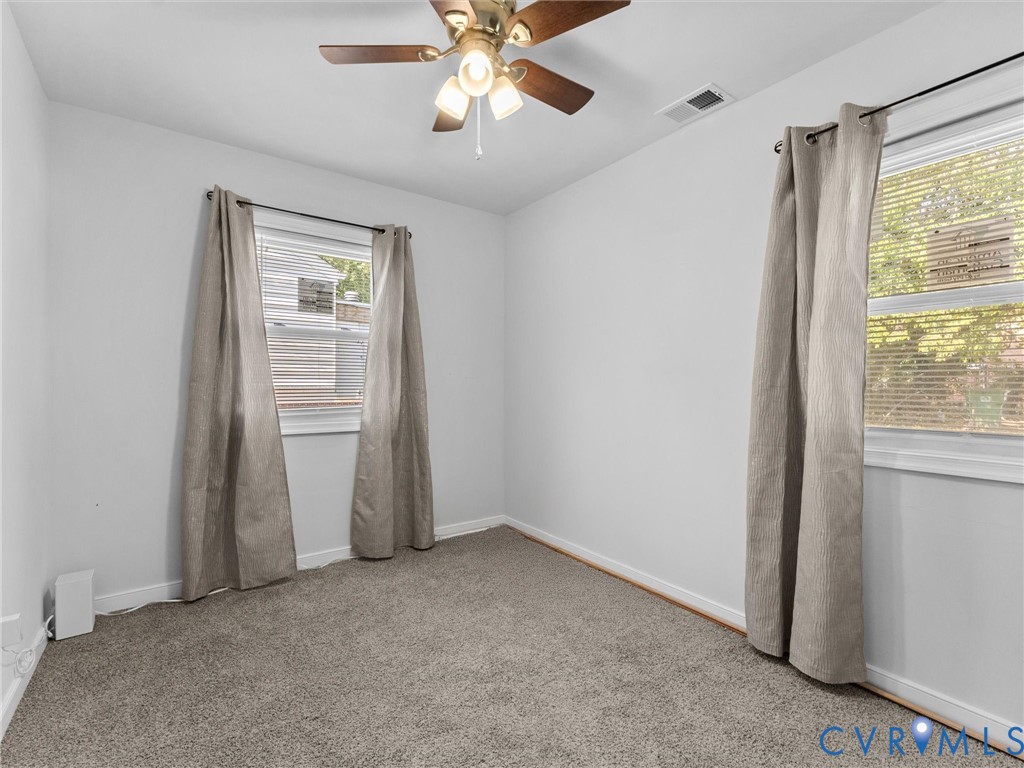 Neutral-toned carpeted flooring, two windows with horizontal blinds, and a ceiling-mounted light fixture with a fan