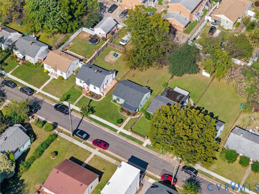 Aerial perspective featuring a residential lot with a grassy backyard, mature shade trees, and perimeter fencing