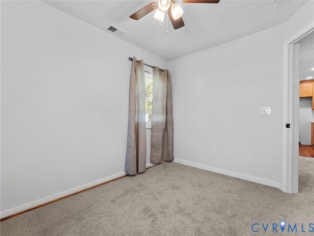 Neutral interior room featuring neutral carpeting and a ceiling-mounted light fixture with a central fan