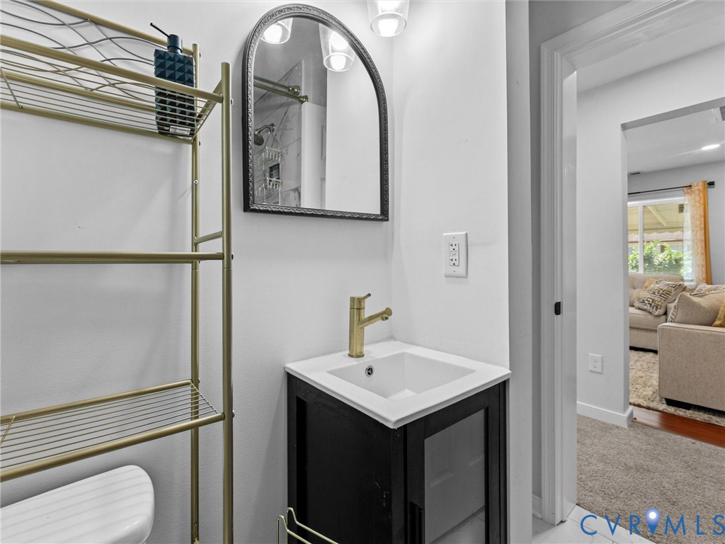 Black vanity with a white countertop and square basin, brass-finish faucet, arched mirror with a dark frame, and wall-mounted light fixtures