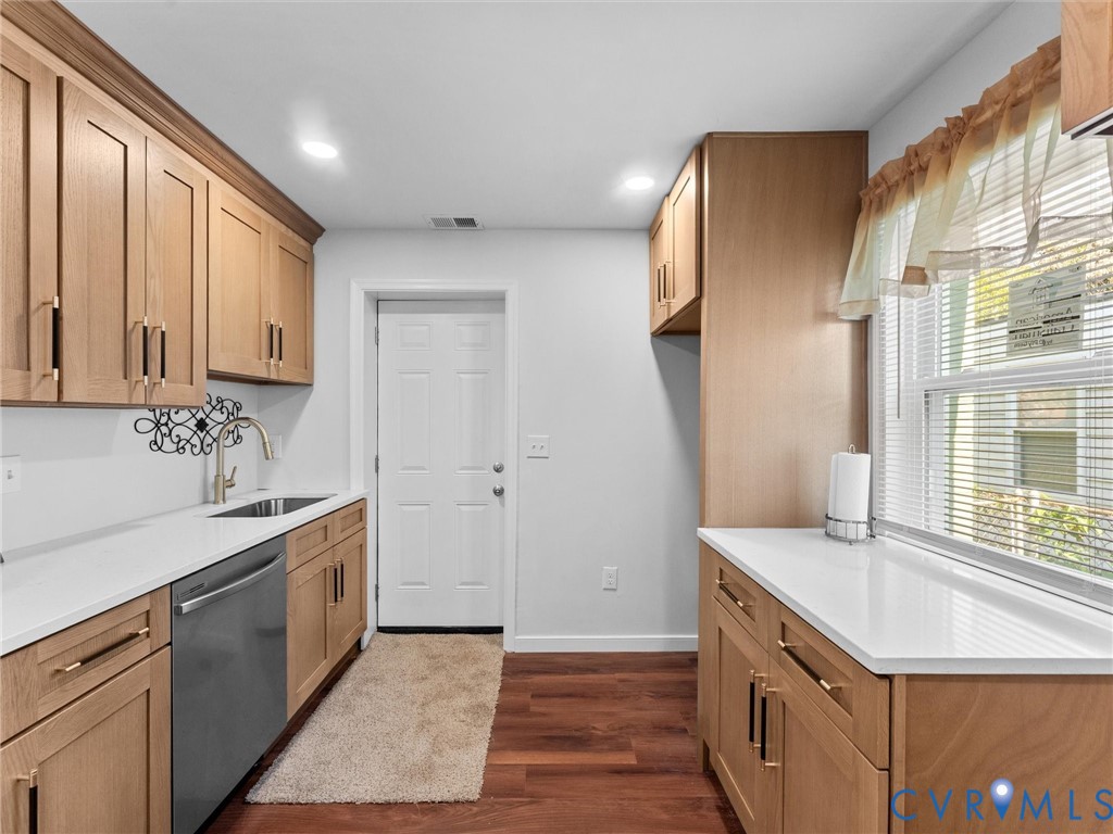 Light wood-finish cabinetry, quartz countertops, stainless steel dishwasher, undermount kitchen sink, and wood-finish flooring