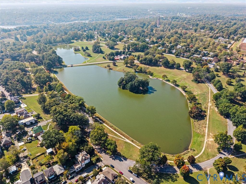 Aerial perspective featuring a large lake, central island, surrounding green space, paved pathways, and mature trees