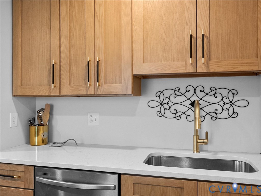 Flat-panel wood-finish cabinetry featuring black and gold bar pulls, solid-surface countertop, undermount stainless steel sink, and high-arch gold-finish faucet