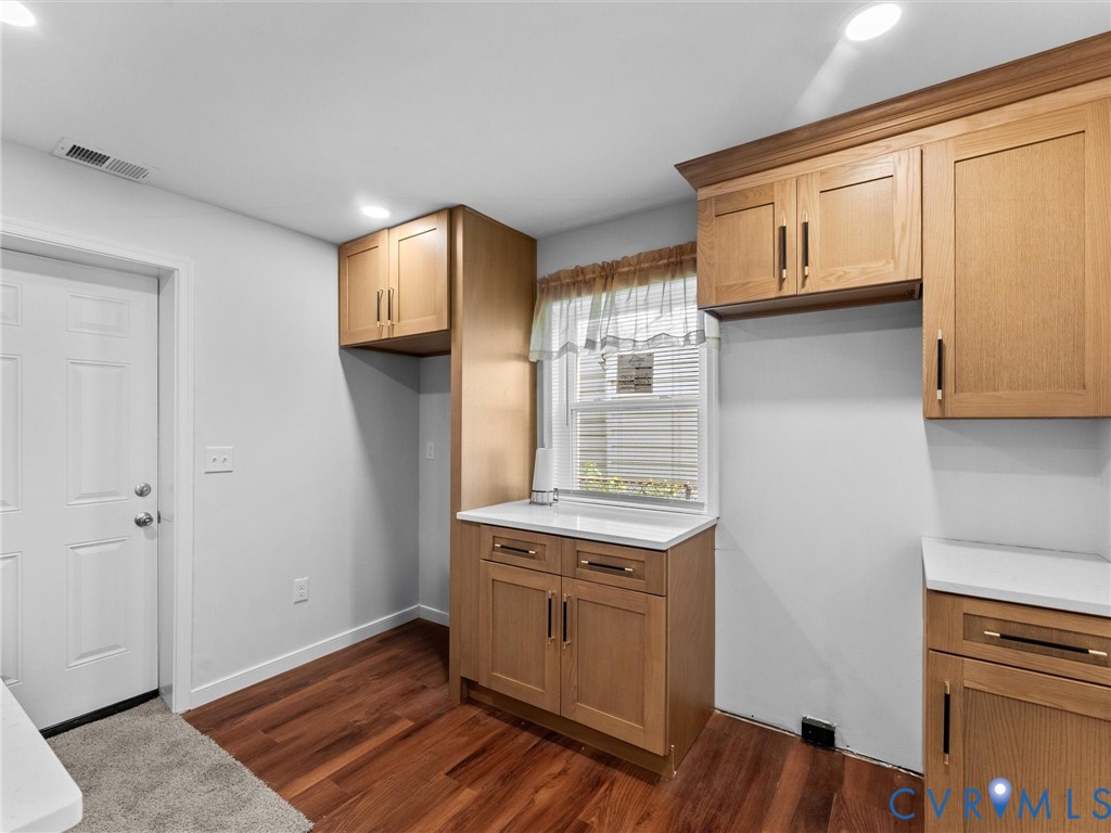 Natural wood-finish cabinetry featuring matte black hardware, white solid-surface countertops, and wood-finish flooring