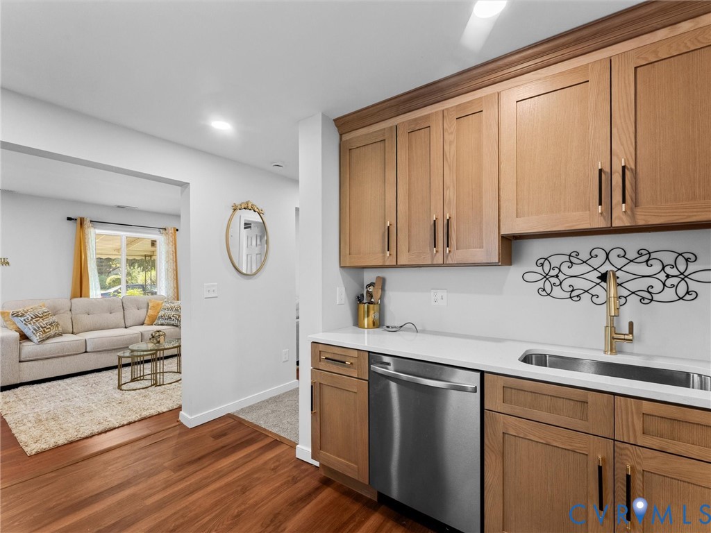 Kitchen area featuring shaker-style wood cabinetry, stone-finish countertops, stainless steel dishwasher, and metallic hardware, complemented by wood-finish flooring
