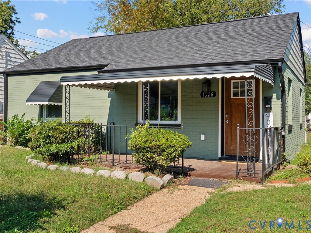 Brick exterior with a covered front porch, decorative metal railings, an awning, and a wooden front door featuring a glass inset