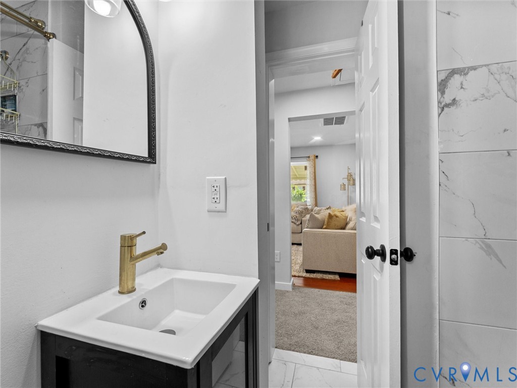 Bathroom vanity with a white rectangular sink, brass-tone faucet, and arched framed mirror, accented by wall-mounted lighting and large-format tile wall surrounds