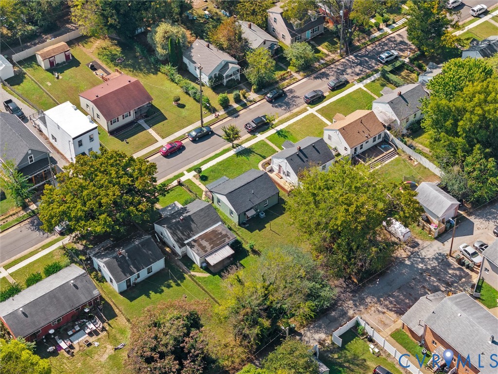 Aerial perspective of a detached residential property featuring a green-toned exterior, asphalt shingle roof, established shade trees, and a grass-covered backyard