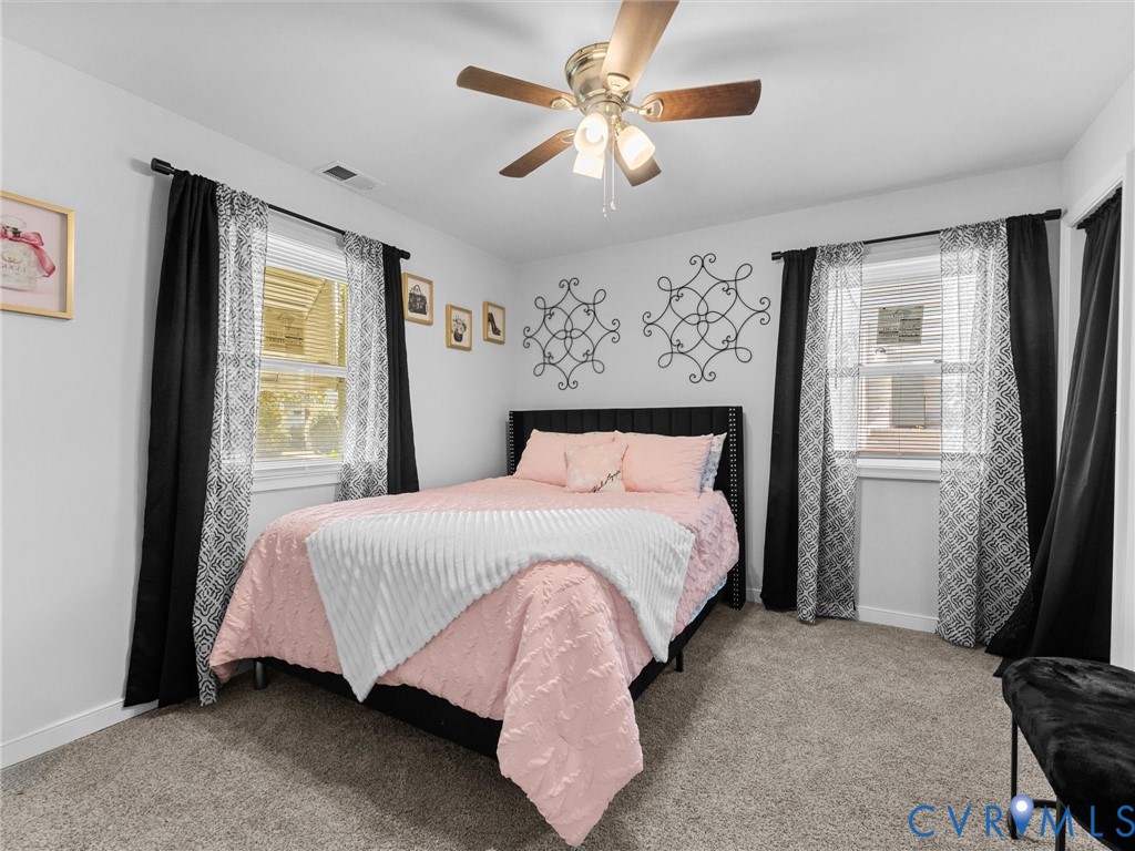 Bedroom interior featuring neutral wall-to-wall carpeting, dual windows, and a multi-blade ceiling fan with an integrated light fixture