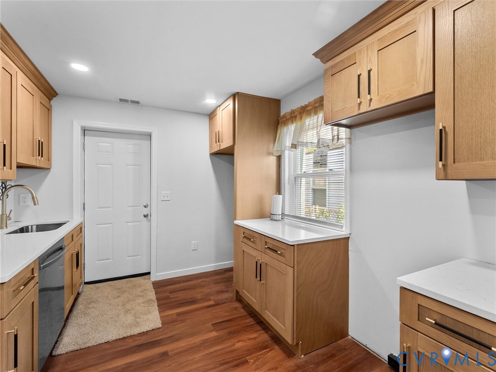 Light wood cabinetry featuring matte black hardware, white solid-surface countertops, wood-finish flooring, and a stainless steel undermount sink