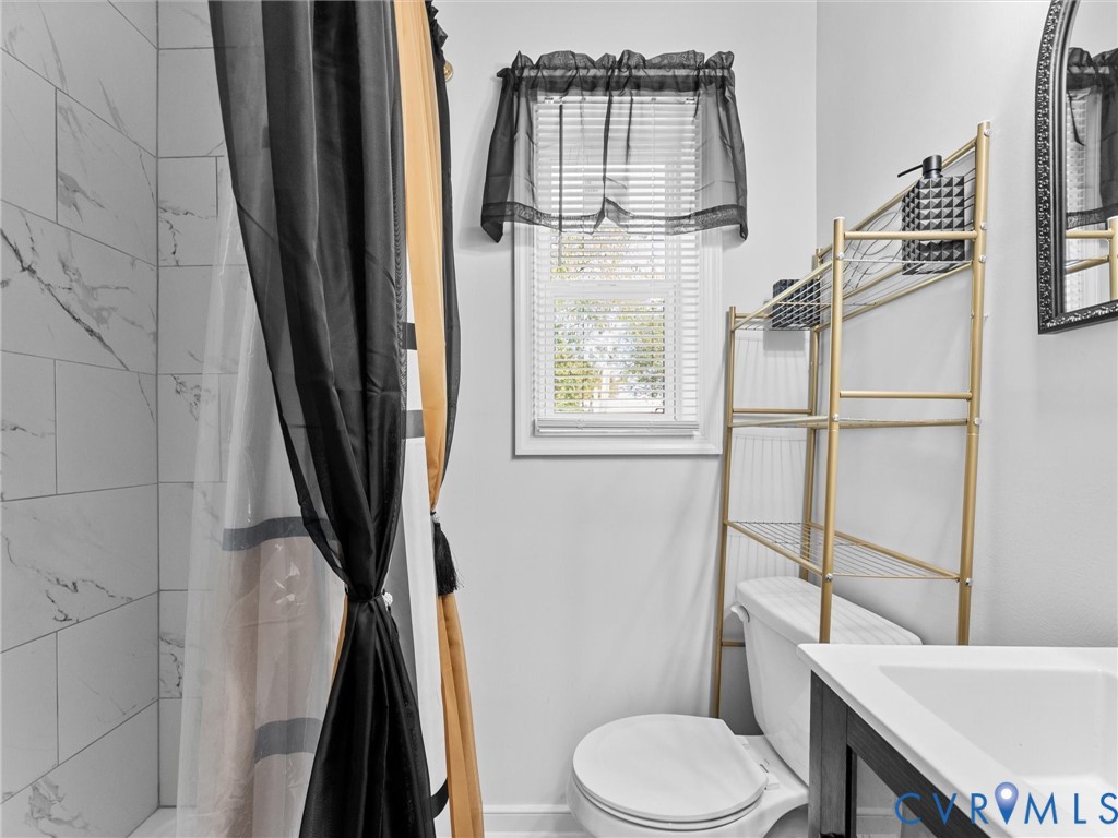 Shower enclosure with large-format tile surround, single-basin vanity with a white countertop, and a window with horizontal blinds