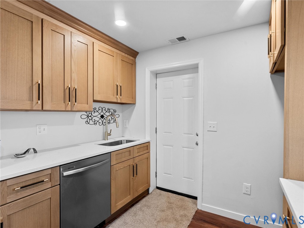 Light wood cabinetry with matte black hardware, solid-surface countertops, undermount stainless steel sink, pull-down faucet, and integrated stainless steel dishwasher