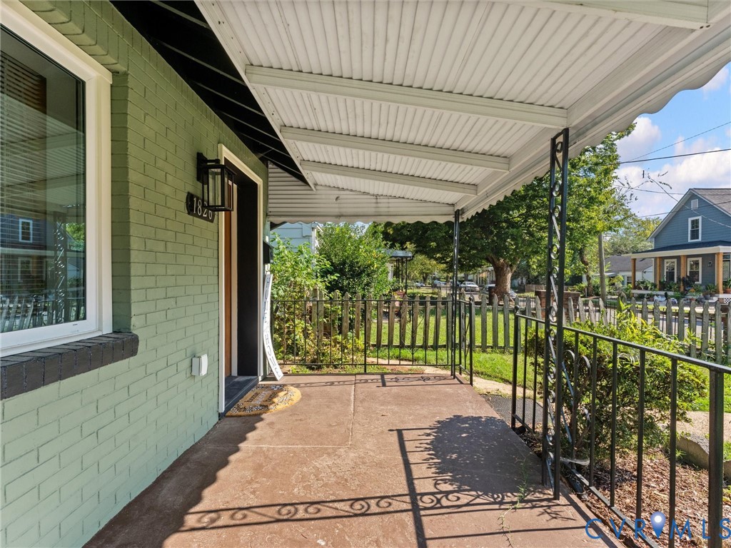 Covered front porch featuring a concrete floor, decorative metal railings, and a green painted brick exterior