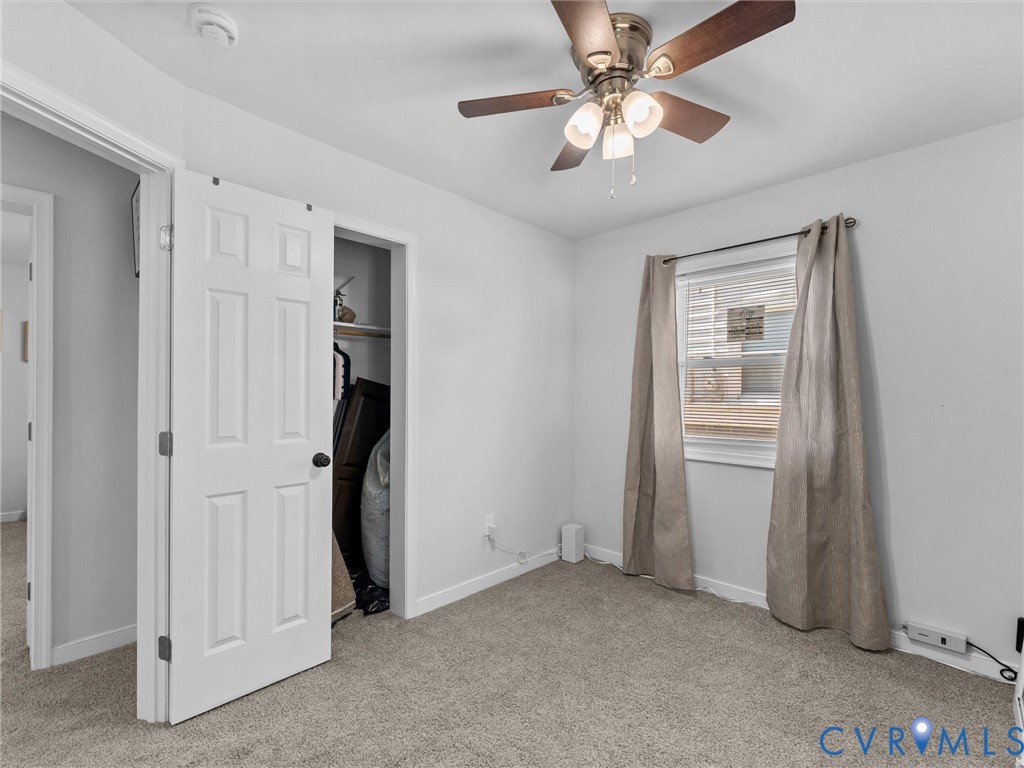 Room featuring carpeted flooring, neutral wall coloring, a multi-blade ceiling fan with integrated lighting, a single-window configuration, and a built-in closet with a swinging paneled door