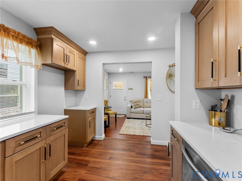 Kitchen featuring light-tone wood cabinetry, solid-surface white countertops, recessed lighting, and wood-finish flooring