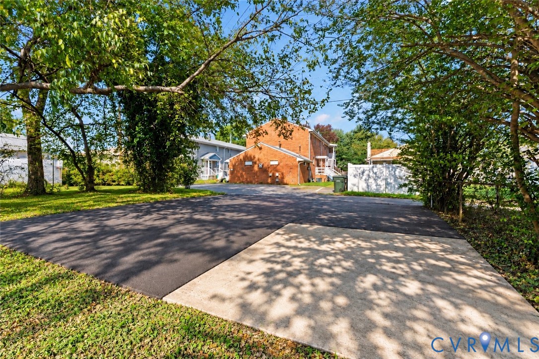 Paved off-street parking area with asphalt and concrete surfaces, surrounded by mature trees and a privacy fence