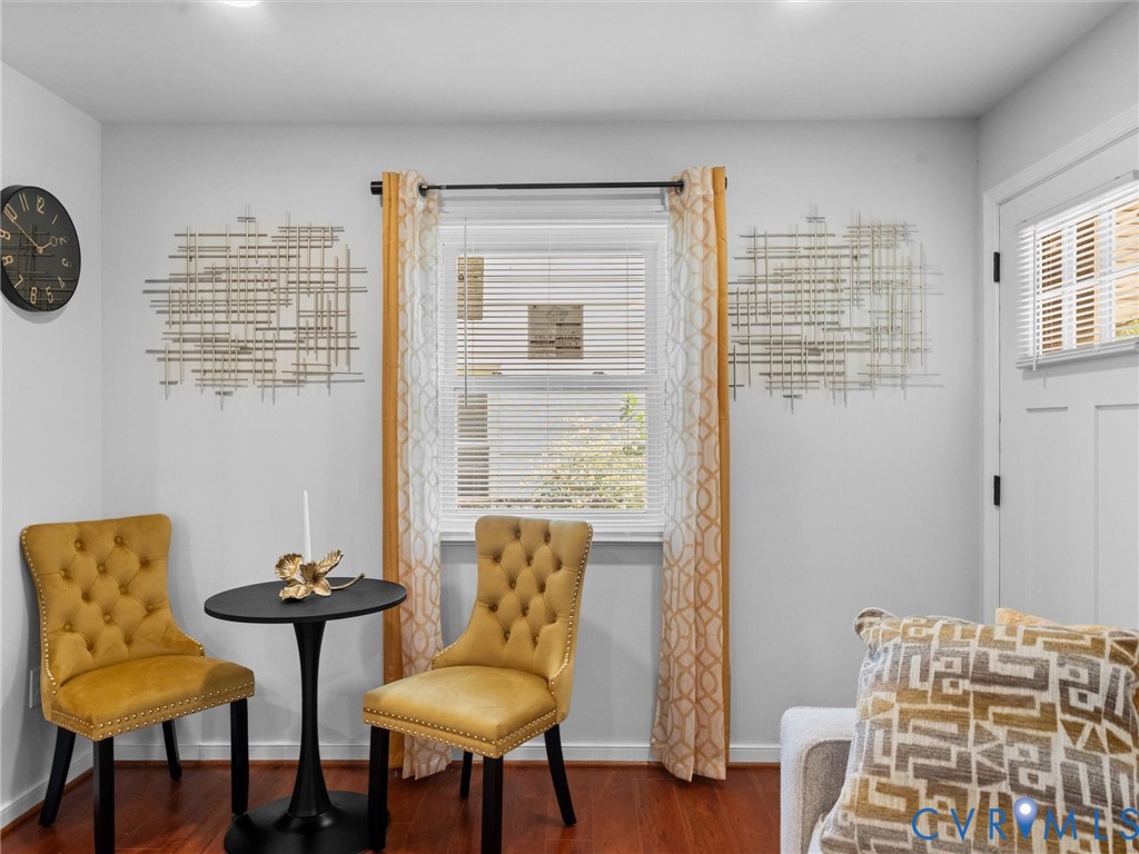 Interior space featuring wood-finish flooring, a double-hung window with horizontal blinds, and a white six-panel door with recessed molding