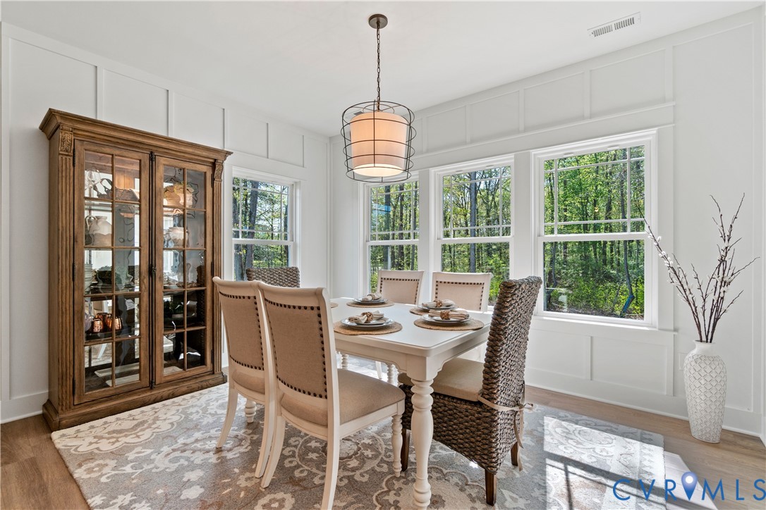Dining area featuring board and batten wall detailing, large windows, wood-finish flooring, and a metal-frame pendant light fixture
