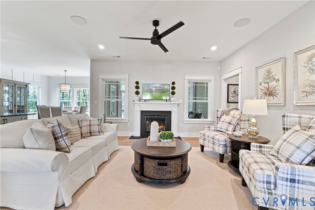Living area featuring a fireplace with a white mantel, ceiling-mounted fan, recessed lighting, and large windows with white trim