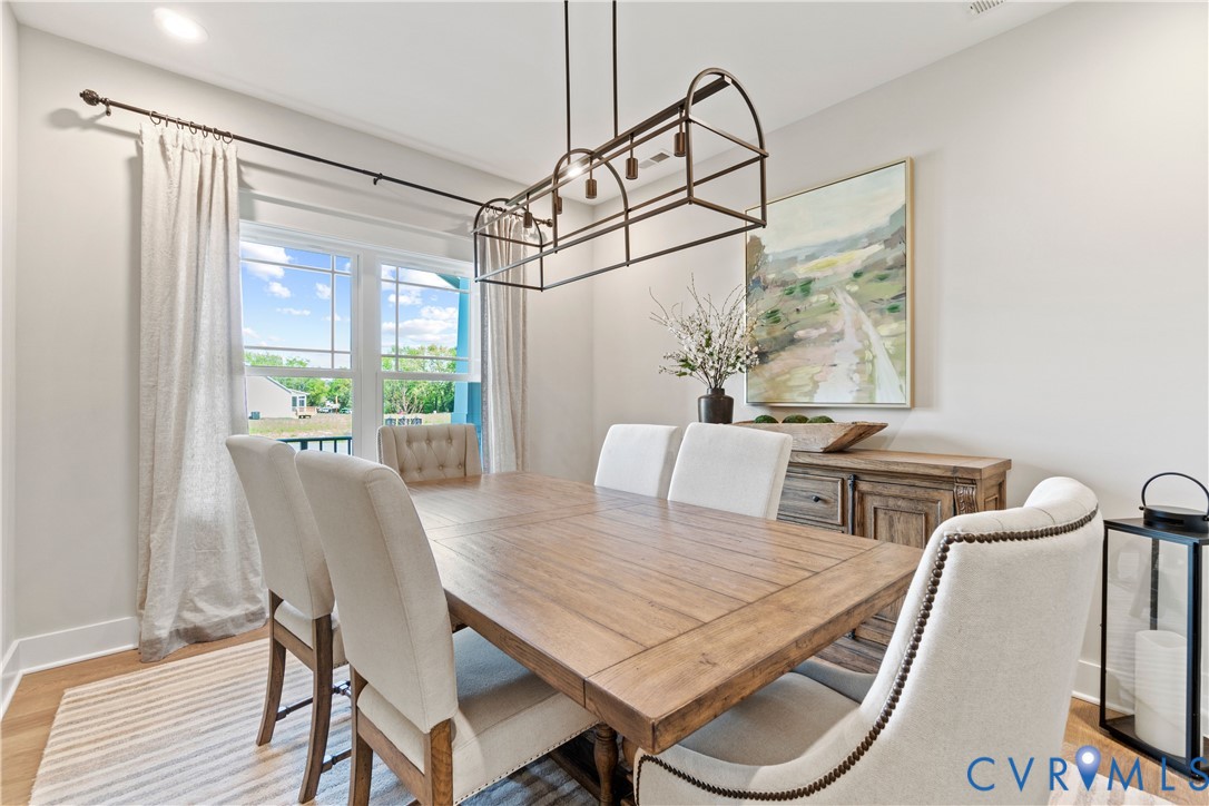 Dining area featuring large windows, wood-finish flooring, and a decorative industrial-style rectangular pendant light fixture
