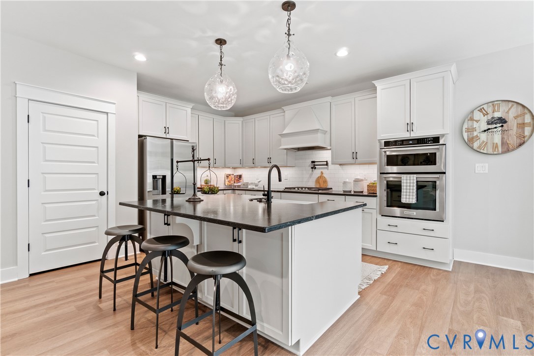 Kitchen featuring white shaker-style cabinetry, dark stone-finish island countertop, built-in double wall ovens, recessed lighting, and glass pendant fixtures
