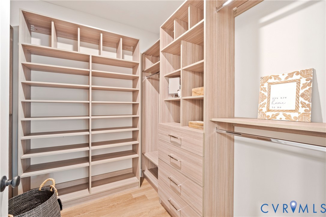 Custom walk-in closet featuring light wood-finish cabinetry, floor-to-ceiling shelving, integrated hanging rods, and built-in dresser drawers