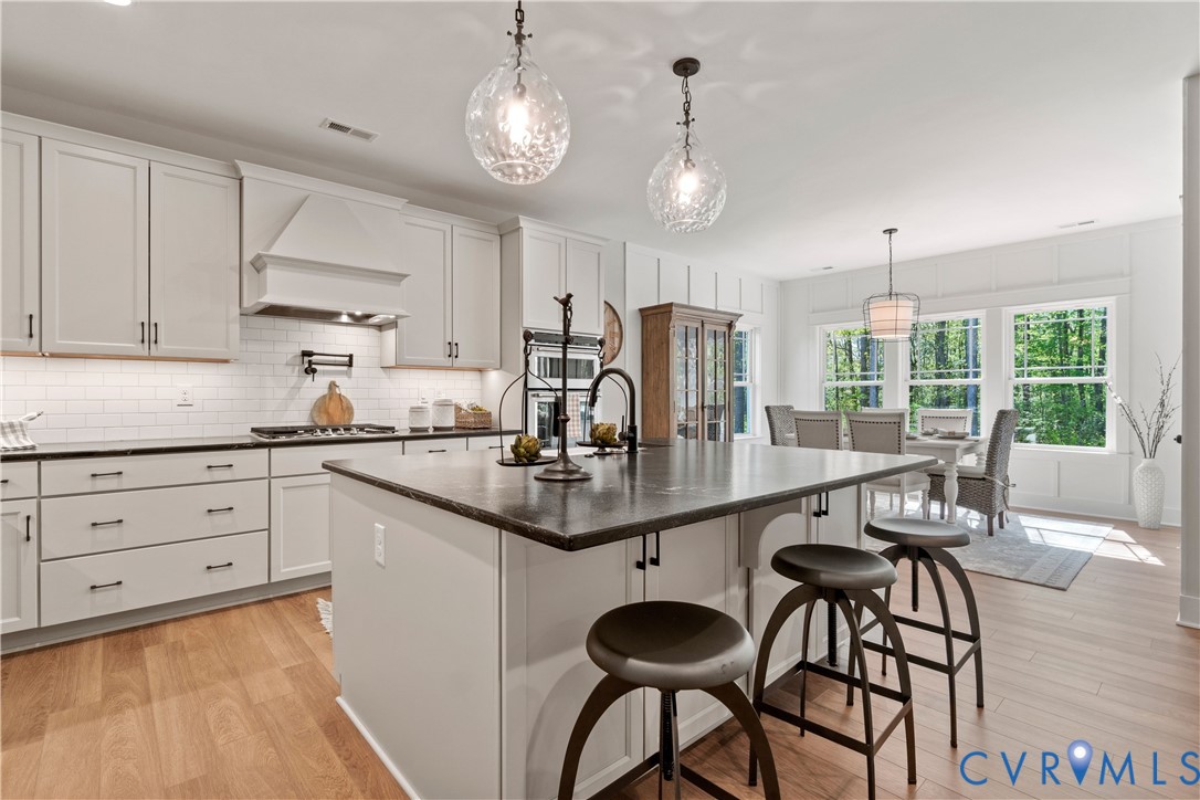 Kitchen featuring white shaker-style cabinetry, quartz countertops, a central island, subway tile backsplash, and wood-finish flooring