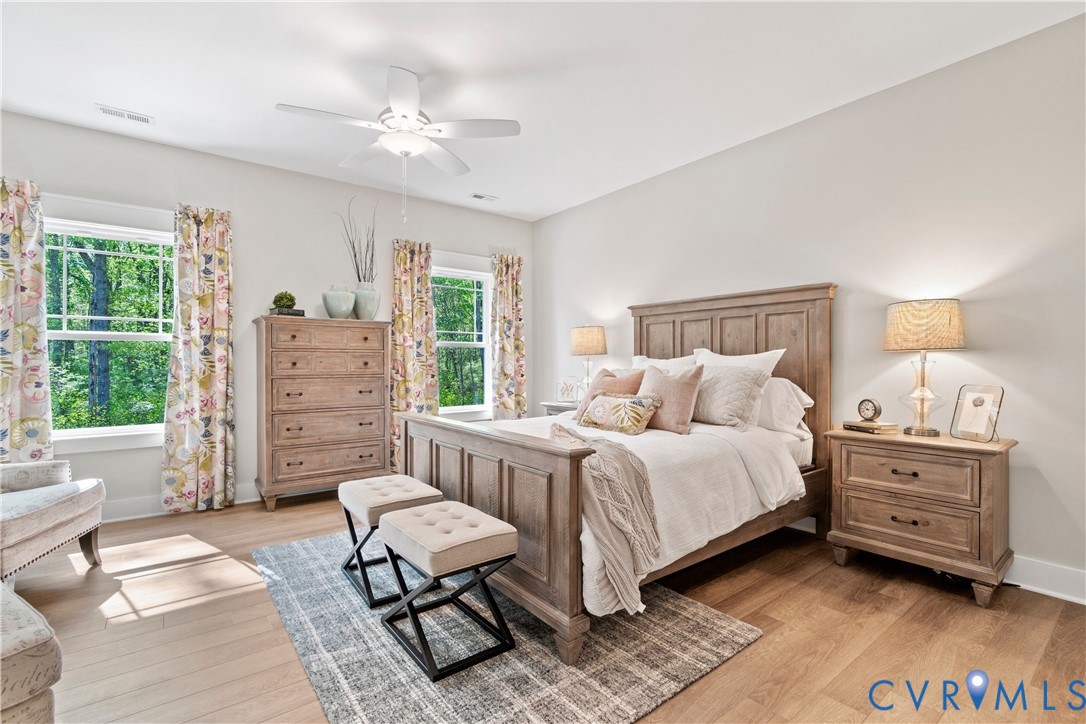 Bedroom featuring wood-finish flooring, dual windows with exterior greenery, and a ceiling-mounted light fixture with fan blades