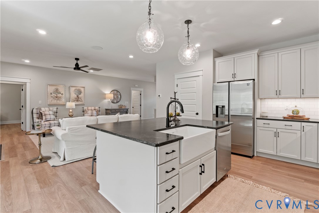 Kitchen featuring an island with a white farmhouse-style sink, dark countertop, shaker-style cabinetry, wood-finish flooring, and dual globe pendant lighting