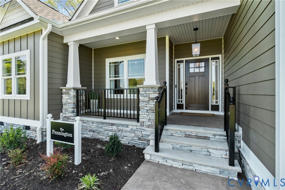 Covered front porch featuring a stacked stone foundation, tapered columns, black metal railings, and a wood-finish front door with sidelights