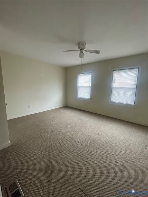 Neutral-toned interior featuring wall-to-wall carpeting, two windows with blinds, and a ceiling fan