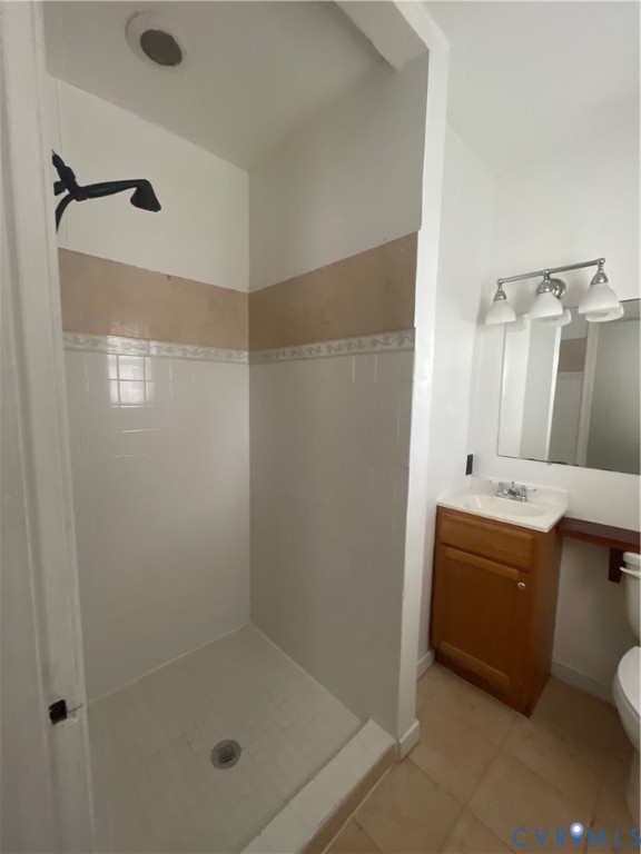 Walk-in shower with tile surround, wood-finish vanity with integrated sink, three-light fixture, and ceramic tile flooring