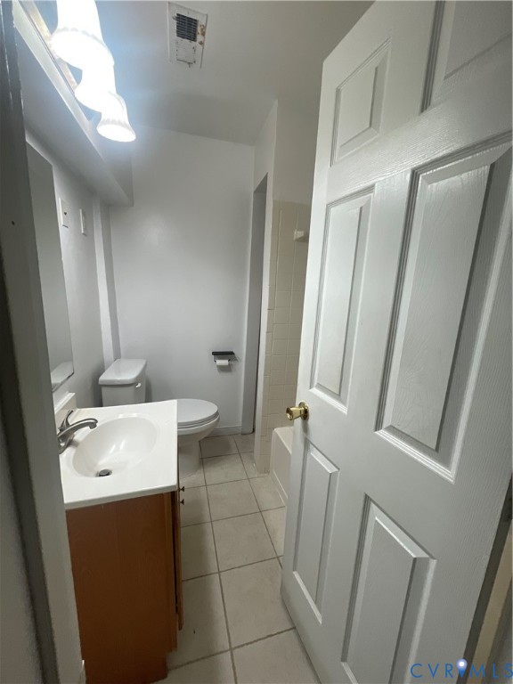 Bathroom featuring a vanity with a white countertop and oval basin, tile flooring, wall-mounted light fixture, and a white six-panel door