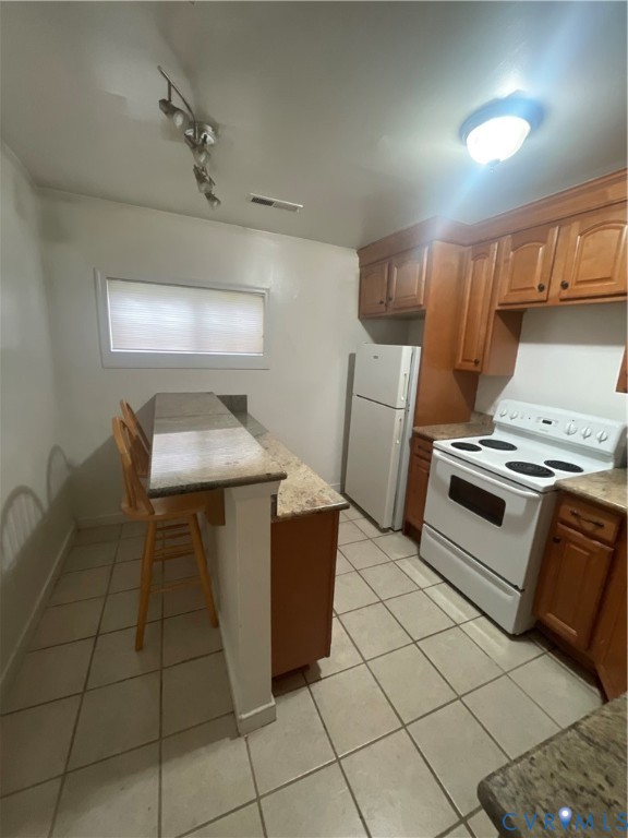 Kitchen featuring stone-finish countertops, raised-panel wood cabinetry, white electric range, and tiled flooring
