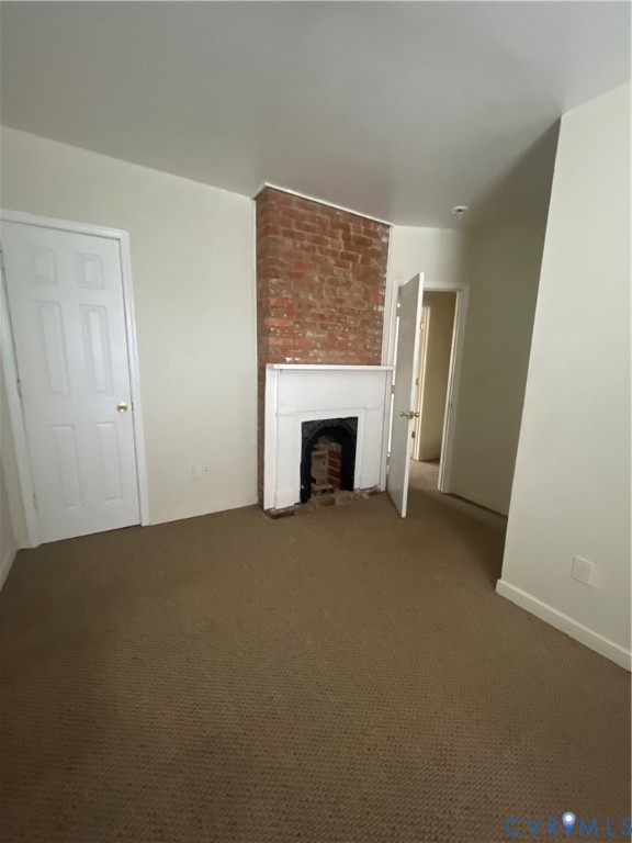 Exposed brick chimney breast featuring a traditional white millwork mantel and fireplace insert, complemented by neutral-tone carpeting and multi-panel interior doors