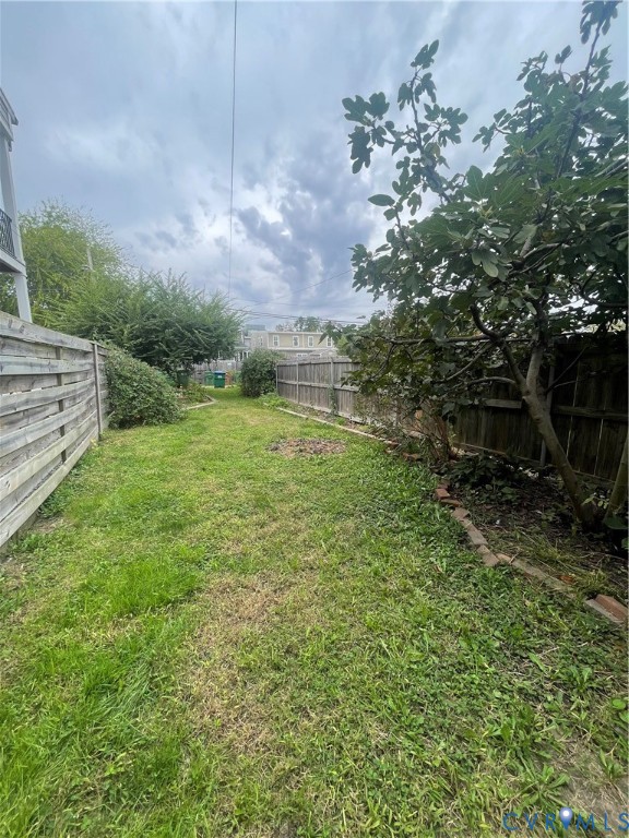 Rear yard featuring a grass lawn, horizontal wood fencing, and mature trees