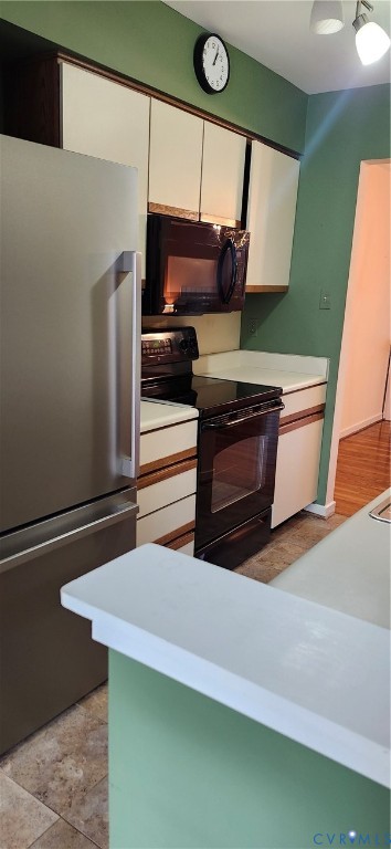 Kitchen featuring cabinetry with wood-tone accents, white countertops, a stainless steel refrigerator, and black built-in oven and microwave