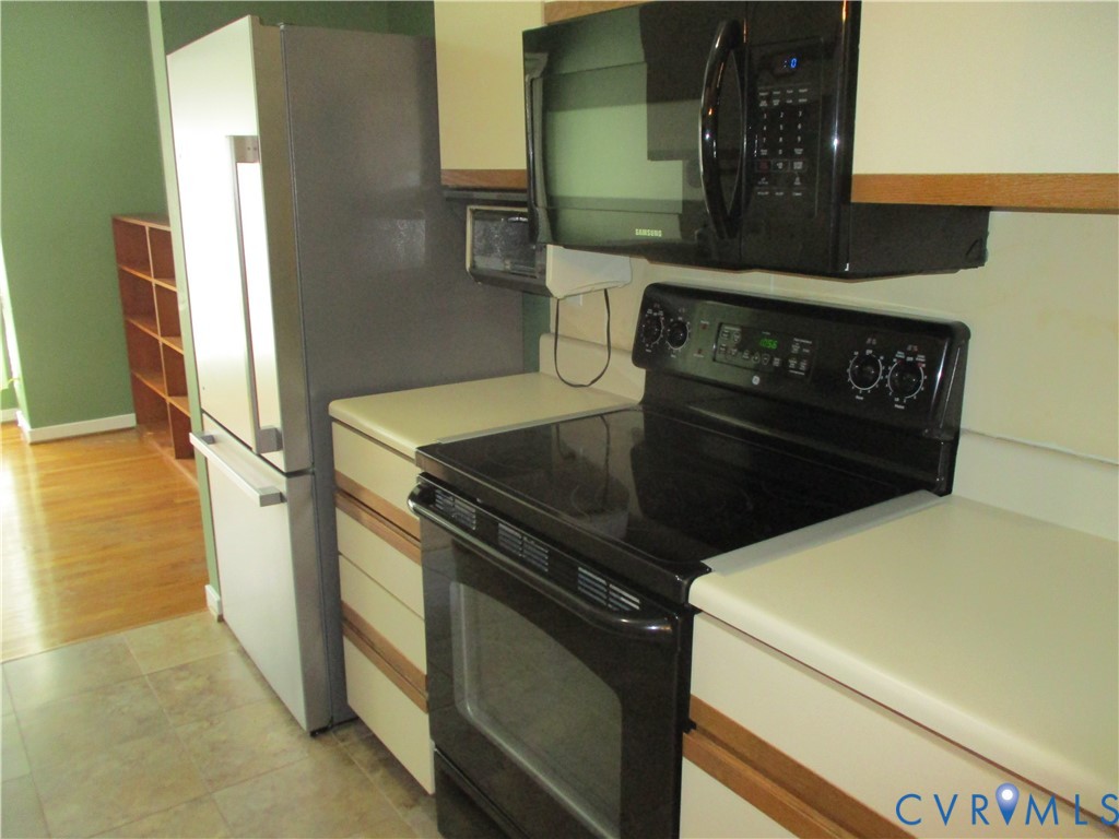 Kitchen featuring a stainless steel refrigerator, black electric range, black over-the-range microwave, solid-surface countertops, and wood-finish flooring