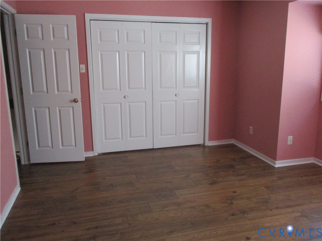 Room interior featuring wood-finish flooring, double-panel closet doors, and a standard interior swinging door