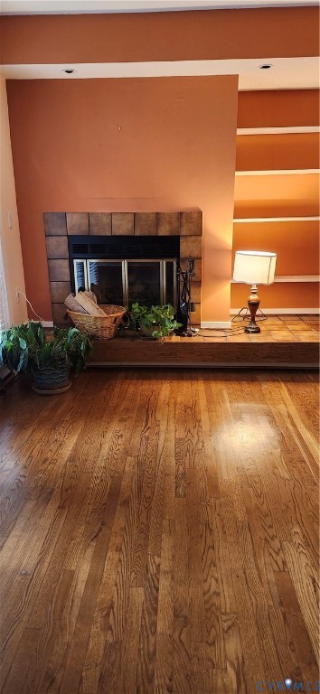 Wood-finish flooring, tiled fireplace surround, raised hearth, and built-in shelving