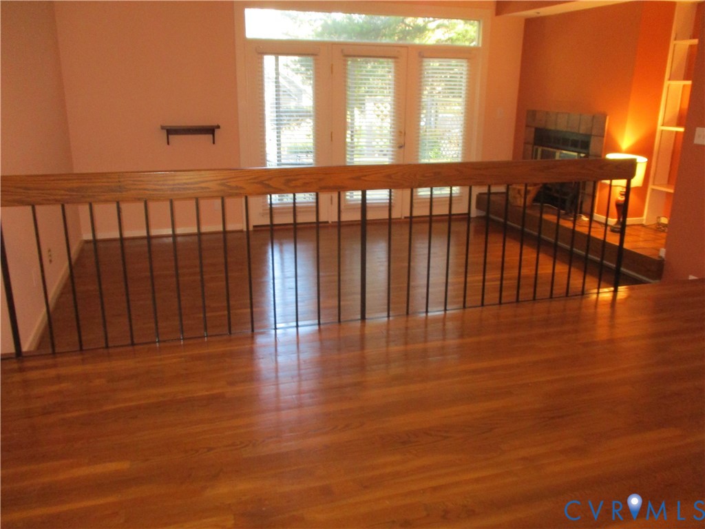 Wood-finish flooring, fireplace with a tiled surround, built-in shelving, wood-capped metal handrail, and glass-paneled double doors