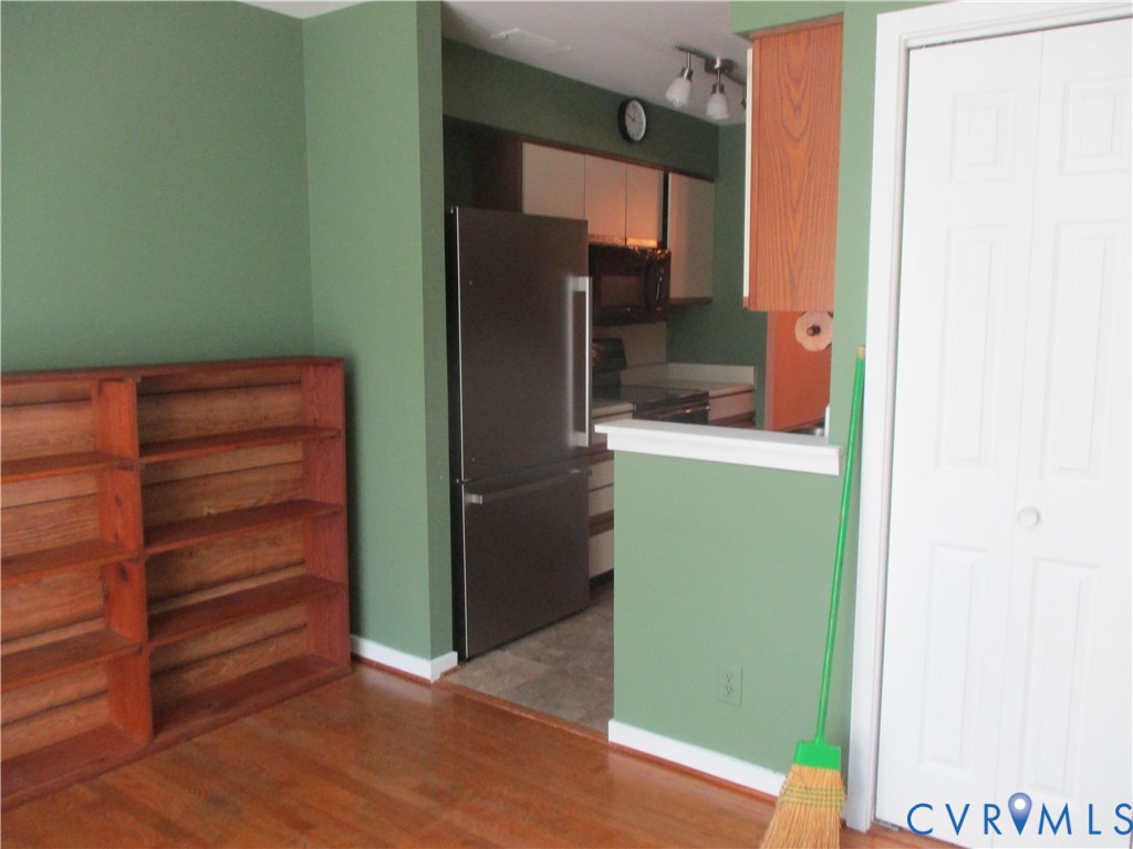Built-in wood shelving unit, wood-finish flooring, stainless steel refrigerator, white-panel closet door, and kitchen cabinetry